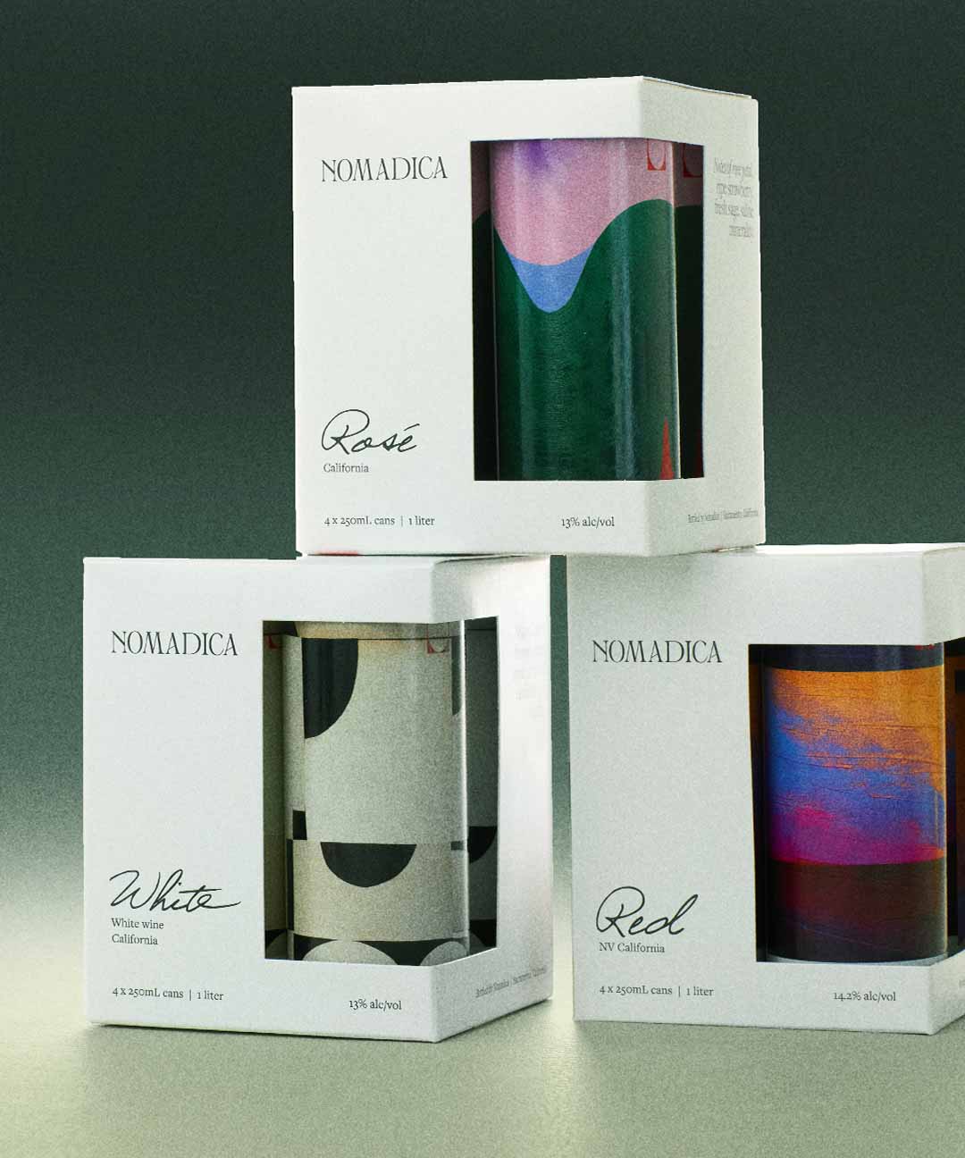 Nomadica wine cans in white, red, and rosé boxes with artistic designs.